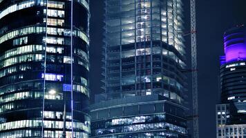 Skyscraper at construction process by night. Modern high-rise building under construction next to glass skyscrapers by night. photo