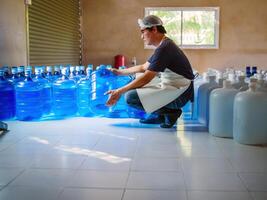 Young man worker or quality inspector in workwear working in checking drinking water gallon in drink water factory before shipment.drinking water business,small business,store,warehouse photo
