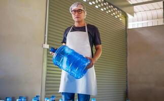 Asian man worker or quality inspector in workwear working in checking drinking water Blue gallon in drink water factory before shipment.drinking water business,small business,store,warehouse photo