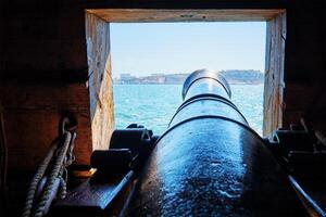 View out of a gunport in hull of the ship on the gun deck over the gun cannon muzzle in photo