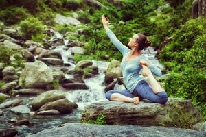 Sorty fit woman doing yoga asana outdoors at tropical waterfall photo