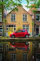 Red car on canal embankment in street of Delft. Delft, Netherlands photo