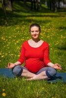 Pregnant woman doing asana Sukhasana outdoors on grass photo