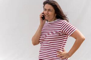 Cheerful middle-aged Caucasian woman with long hair conversing on cellphone in striped top photo