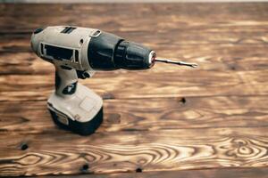 There is a cordless drill on a wooden table. A working tool. DIY concept photo