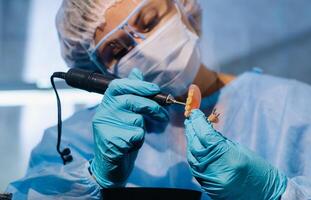 A dental technician in protective clothing is working on a prosthetic tooth in his laboratory photo