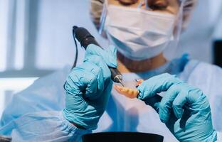 un dental técnico en protector ropa es trabajando en un protésico diente en su laboratorio foto