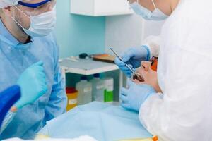 A male dentist with dental tools drills the teeth of a patient with an assistant. The concept of medicine, dentistry and healthcare photo