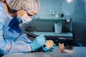 A dental technician in protective clothing is working on a prosthetic tooth in his laboratory photo