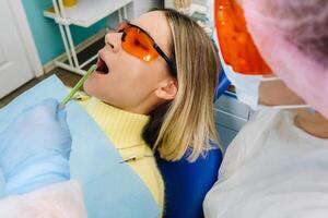 A young beautiful girl in dental glasses treats her teeth at the dentist with ultraviolet light. filling of teeth photo