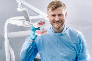 un modelo de un humano mandíbula con dientes y un cepillo de dientes en el del dentista mano foto