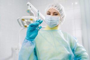 A masked dentist holds an injection syringe for a patient in the office photo