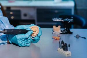 A masked and gloved dental technician works on a prosthetic tooth in his lab photo