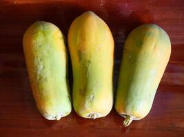 The papaya fruit is almost ripe and is greenish-orange in color, the background is a brown wood pattern photo