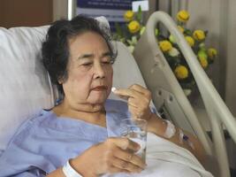 Asian senior  woman lying in hospital bed, taking medicine. Elderly health concept. photo