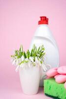 Spring cleaning concept. Detergent, kitchen sponge and spring flowers on a pink background. Close-up. Selective focus. photo