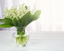 A bouquet of fresh lilies of the valley in a vase on the table. Copy space. Selective focus. photo