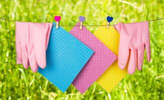 Spring composition with kitchen rags and rubber gloves hanging on a clothesline against the backdrop of green grass. Spring cleaning concept. Close-up. Selective focus. photo