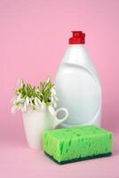 Spring composition with detergent, kitchen sponge and spring flowers on a pink background. Cleaning concept. Close-up. Selective focus. photo