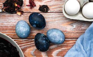 Easter eggs painted with natural hibiscus dye in purple on the wooden table. The process of dyeing eggs with natural food coloring. Close-up. Top view. photo