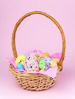 Decorative Easter Eggs in a wicker basket on a pink background. Easter decor. Selective focus. photo