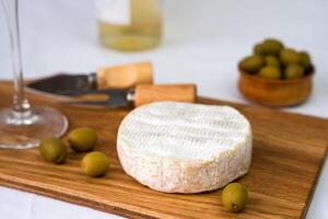 Camembert cheese, olives and a wineglass of wine on a wooden board. Close-up. Selective focus. photo