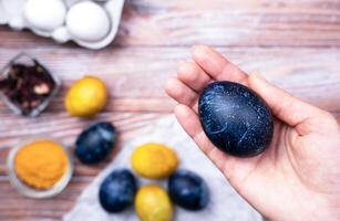 Woman's hand hold blue Easter egg. Coloring eggs for Easter with natural food coloring turmeric and hibiscus tea at home. Close-up. Top view. photo