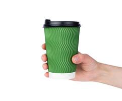 Woman's hand holds green disposable paper cup with cappuccino isolated on white background. Coffee to go. Close-up. Selective focus. photo