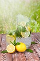 Fresh natural lemonade with lemon slices and fresh mint and ice cubes on wooden table. A refreshing cocktail in the heat of summer. Summer sunny day. Close-up. photo