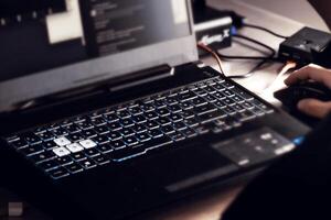 Close up of man's hand using wireless mouse and laptop computer with blue backlit keyboard photo