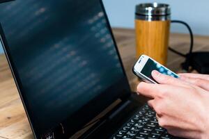 Woman using mobile phone in the office with a laptop and a coffee photo