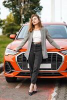 Beautiful girl standing in car front and holding her hands to hood. Young woman photo