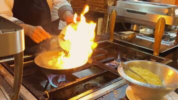 een chef bereidt zich voor pasta in een snel voedsel stijl. de frituren pan is Aan brand. olie dat vangsten brand gedurende Koken video