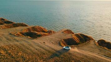 lindo panorama e natureza a partir de a drone. Visão a partir de a zangão em uma branco carro viajando em fora da estrada terreno de a mar. pólen formado atrás a carro enquanto dirigindo. video