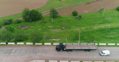 A drone flies over a truck driving on a country road. There are trees and fields around. video