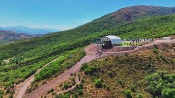 il fuco mosche al di sopra di il montagna funivia stazione. è un' soleggiato estate giorno, circondato di colline coperto con verde. video