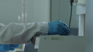 en man i en vit täcka och skyddande handskar Arbetar i en kemisk laboratorium med en vetenskaplig instrument. video