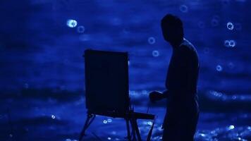 Silhouette of an artist with an easel against the background of an evening river. video