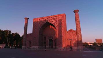 A drone flies near a complex Bibi-Khanym Mosque in Samarkand, Uzbekistan. The building is illuminated by the pink dawn light. Cloudless morning. video