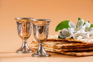 contento Pascua. tradicional judío día festivo. plata vino tazas, primavera flores y matzo un pan foto