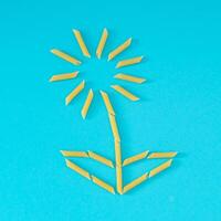 Creative food composition of yellow flower made with pasta penne rigate on bright blue background. Minimal food concept. Creative pasta art background. Flat lay, top of view. photo