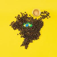 creativo composición hecho con taza de café, mapa de Brasil hecho con asado café frijoles y brasileño bandera en amarillo antecedentes. mínimo disposición. Brasil el parte superior productor de café concepto. plano poner. foto