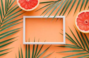 Creative trendy summer composition made of grapefruit and tropical green palm leaves with white frame copy space on orange background. Fruit minimal concept. Exotic nature flat lay. photo