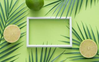 Creative trendy summer composition made of lime and tropical palm leaves with white frame copy space on green background. Fruit minimal concept. Exotic monochromatic flat lay. photo