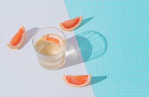 Summer scene made with refreshing drink with slices of fresh grapefruit on white and blue background. Sun and shadows. Minimal cocktail concept. Trendy summertime party idea. Summer aesthetic. photo