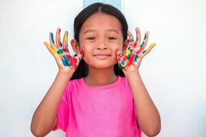 Cute little girl with colorful painted hands on wall background photo