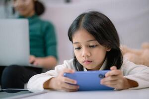 A young girl is playing a game on her phone while her mother works on her laptop photo