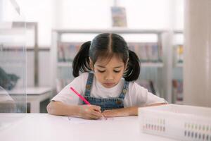 A young girl is sitting at a table with a pencil and a piece of paper photo