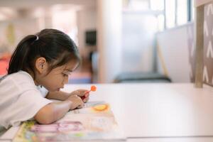 A young girl is sitting at a table reading a book photo