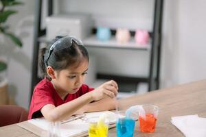 Asian girl making Walking Water experiment. Food color is added to the water in the glass, water moves along the paper, and then color is mixed. Concept of science for kid photo